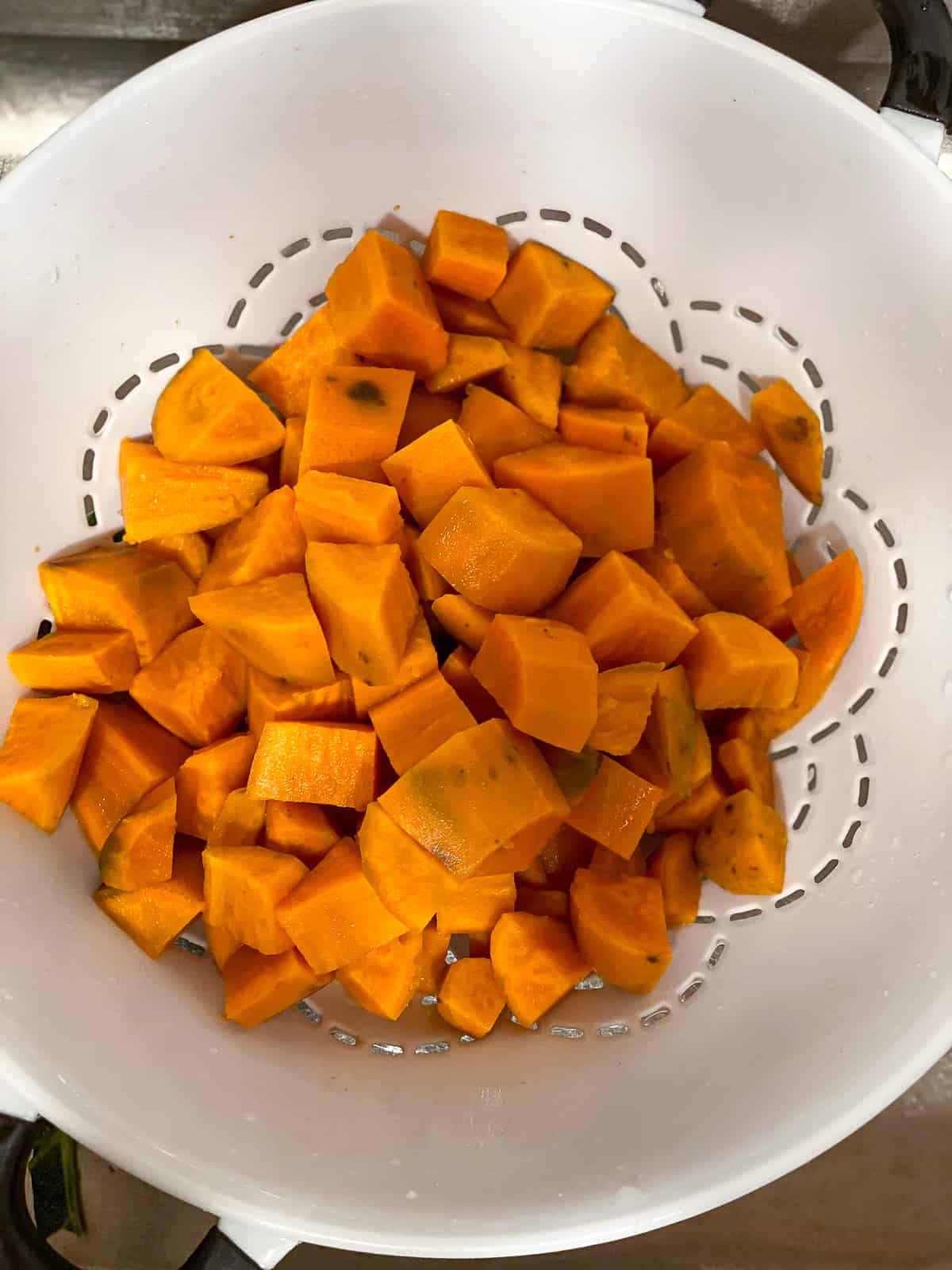 White colander with cooked sweet potatoes.