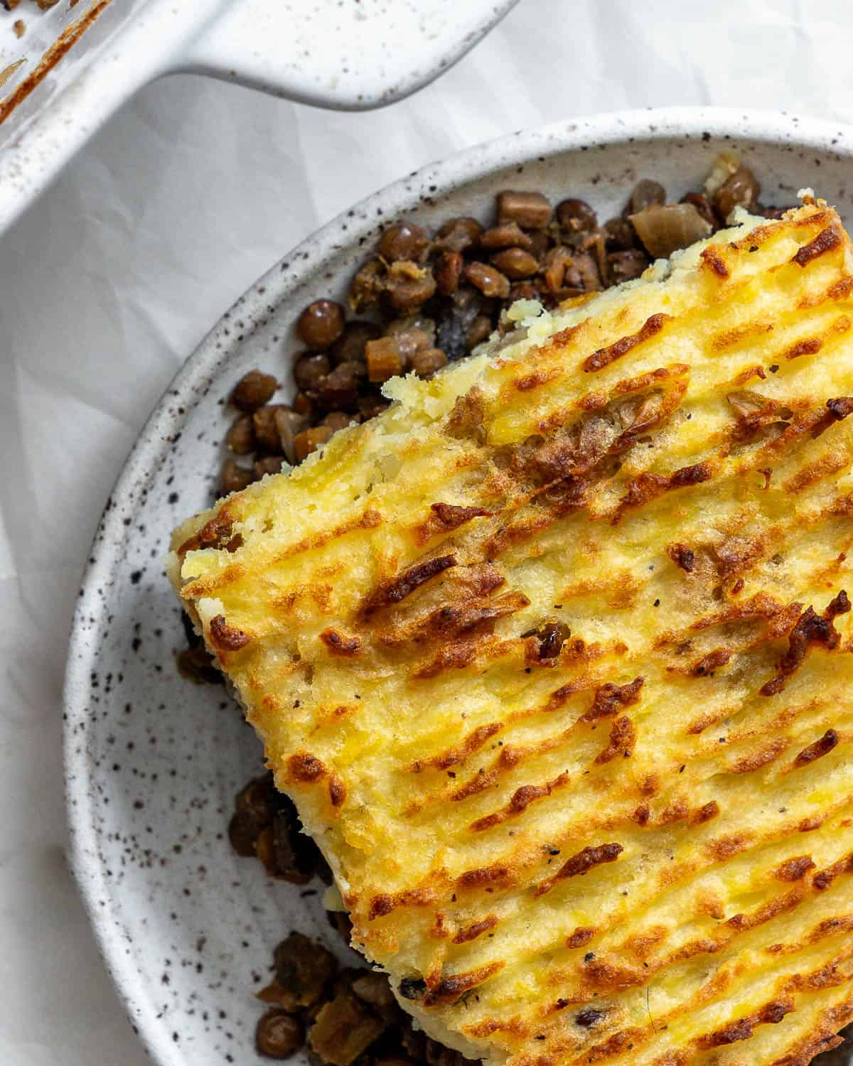 Vegan lentil shepherd's pie in a baking dish with a serving spoon.