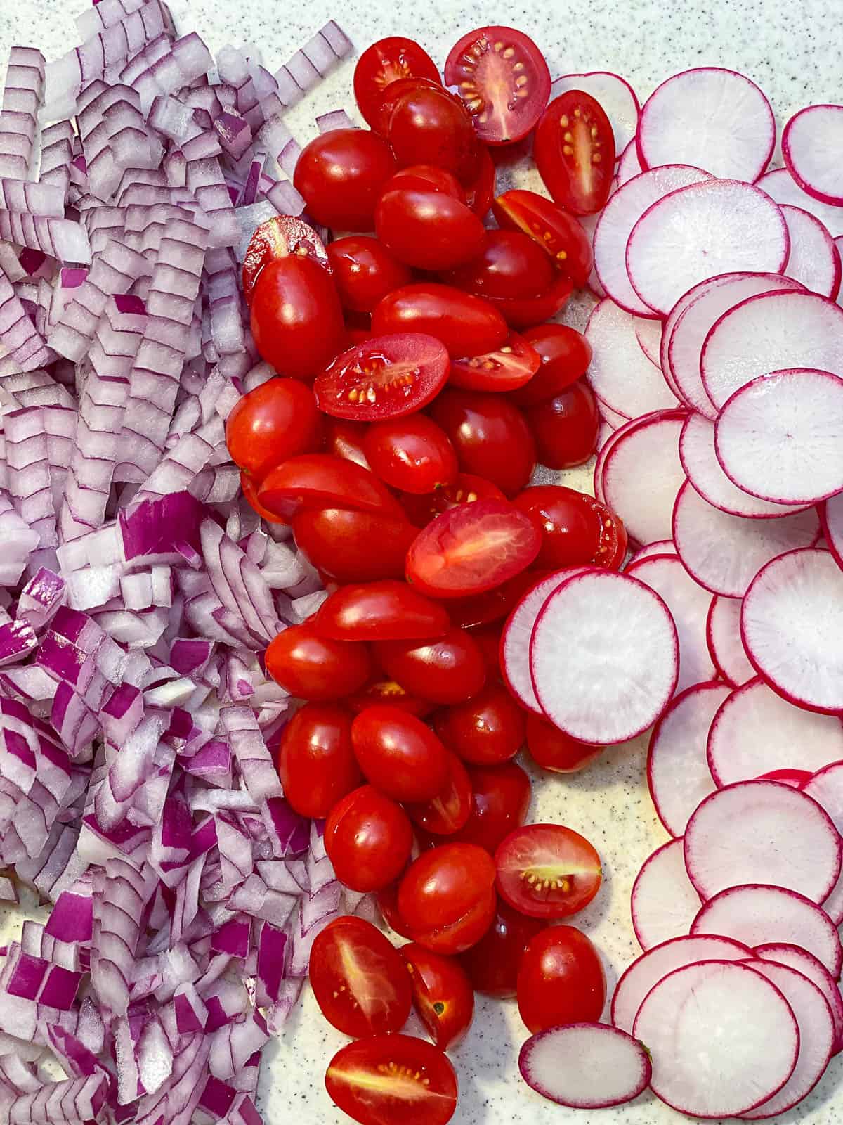 Diced red onion next to halved cherry tomatoes that are next to sliced radishes.