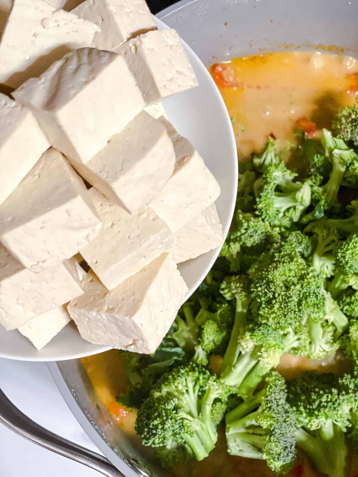 Adding cubed tofu to a pot of mixed veggies and coconut curry.