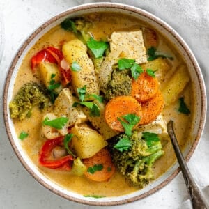 Bowl with Tofu Yellow Curry over a white textured surface with a spoon in it.