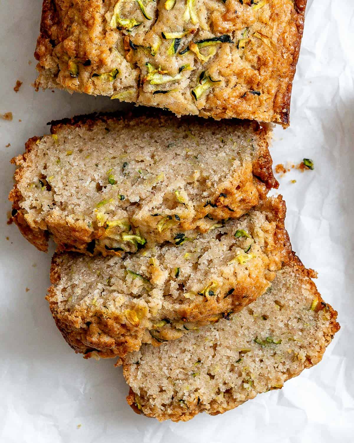 Slices of zucchini bread on white crinkled parchment paper.