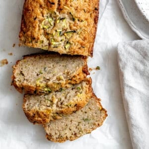 Slices of zucchini bread on white crinkled parchment paper. There's part of a speckled bowl in the top right corner, and part of a gray napkin in the bottom right corner.