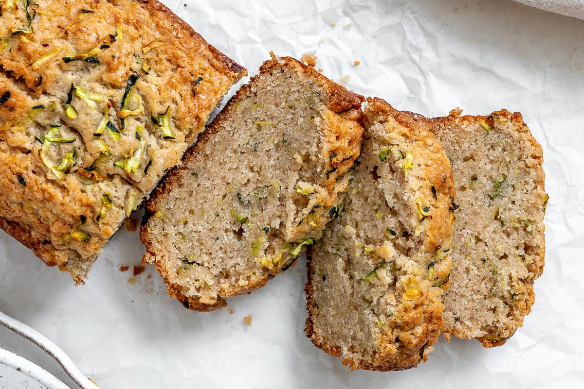 Slices of zucchini bread on white crinkled parchment paper.