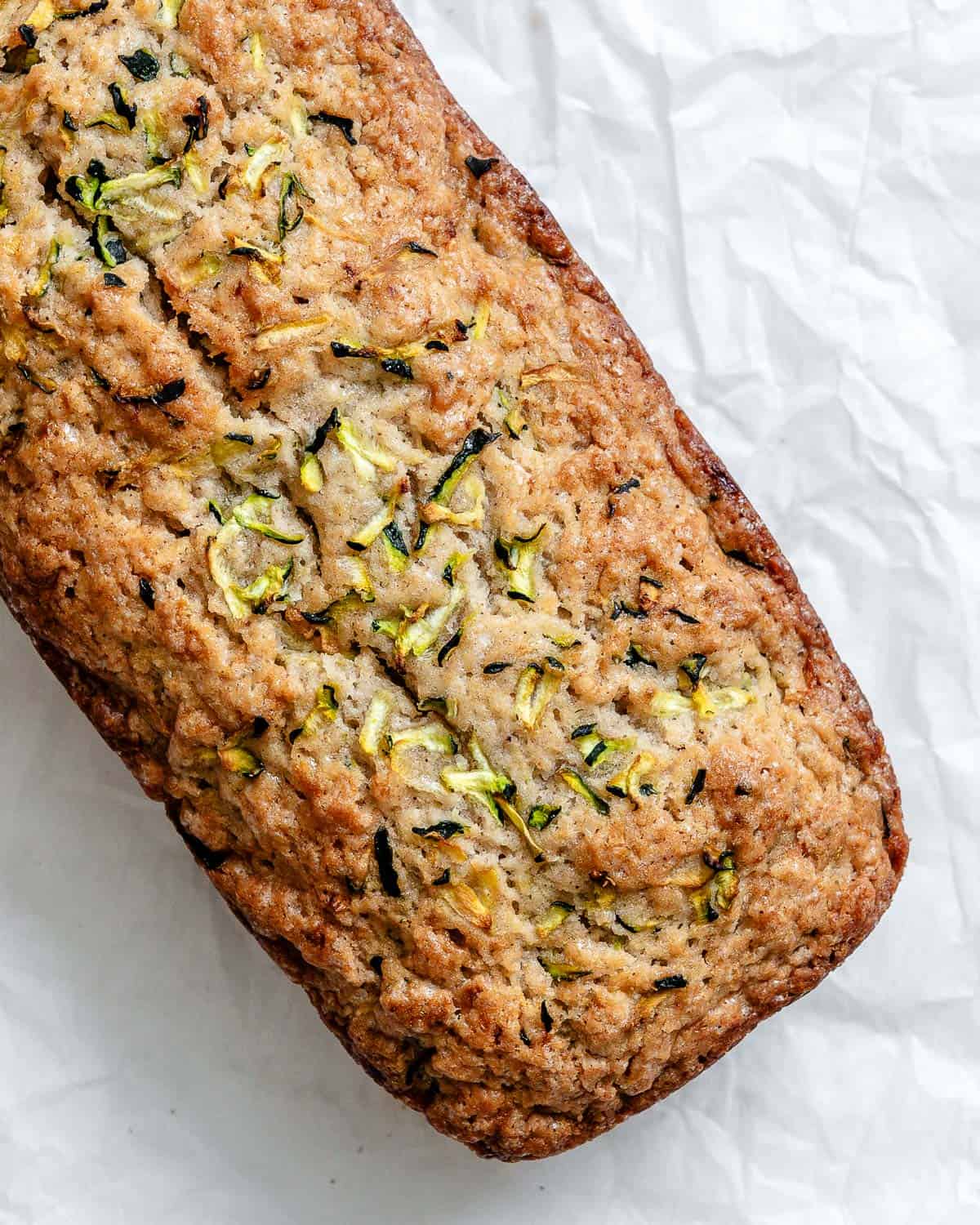 Freshly baked loaf of zucchini bread on top of a white crinkled parchment paper.