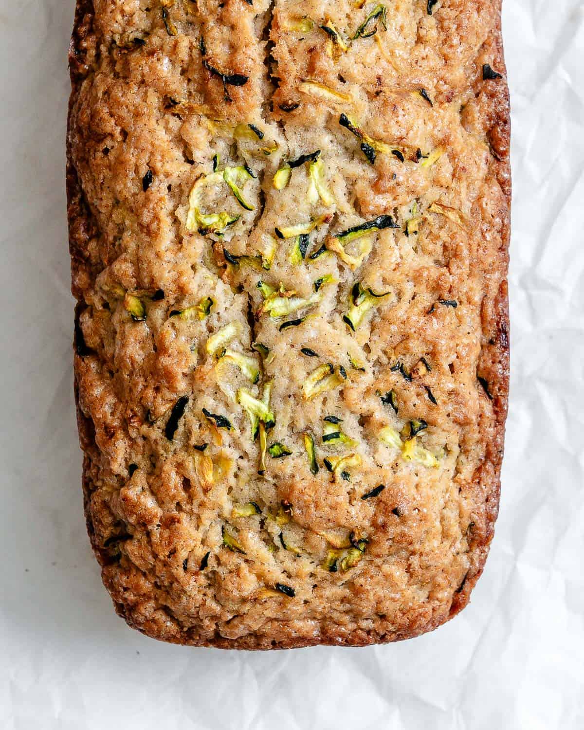 A freshly baked load of zucchini bread on top of a white crinkled parchment paper.