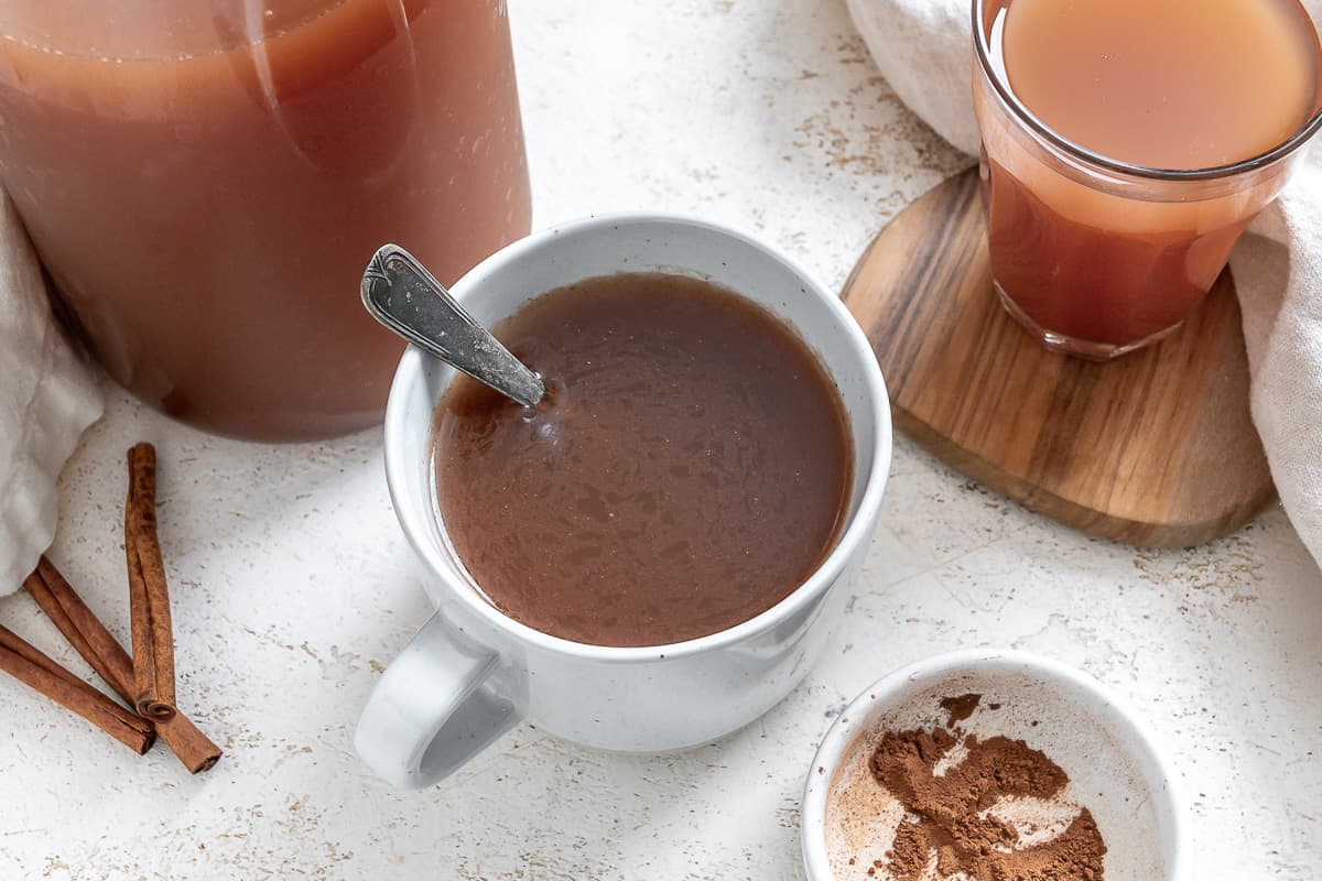 A glass mug of mulled apple cider with a cinnamon stick.
