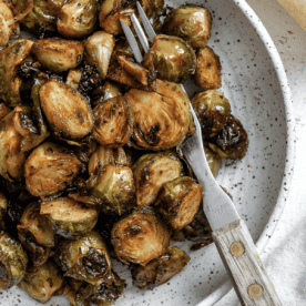 Roasted Brussels sprouts with dark caramelized edges on a speckled plate with a fork.