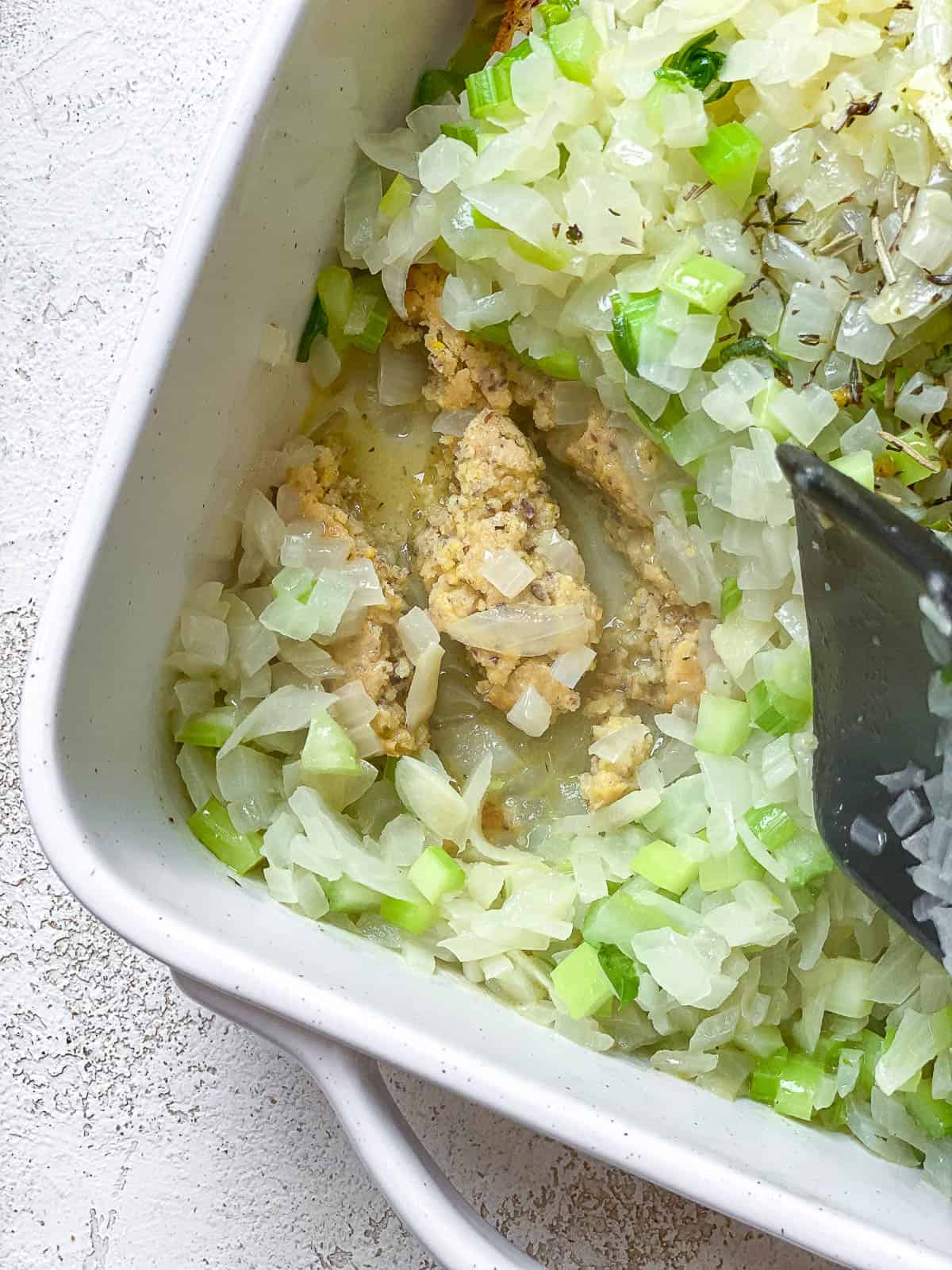 Cornbread stuffing being gently mixed in a baking dish.