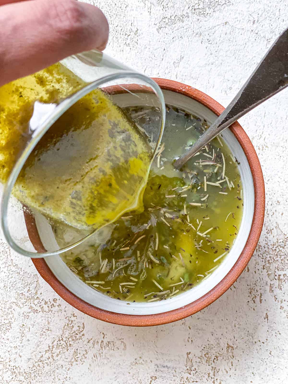 Vegetable broth poured into melted vegan butter and fresh herbs in a glass bowl.