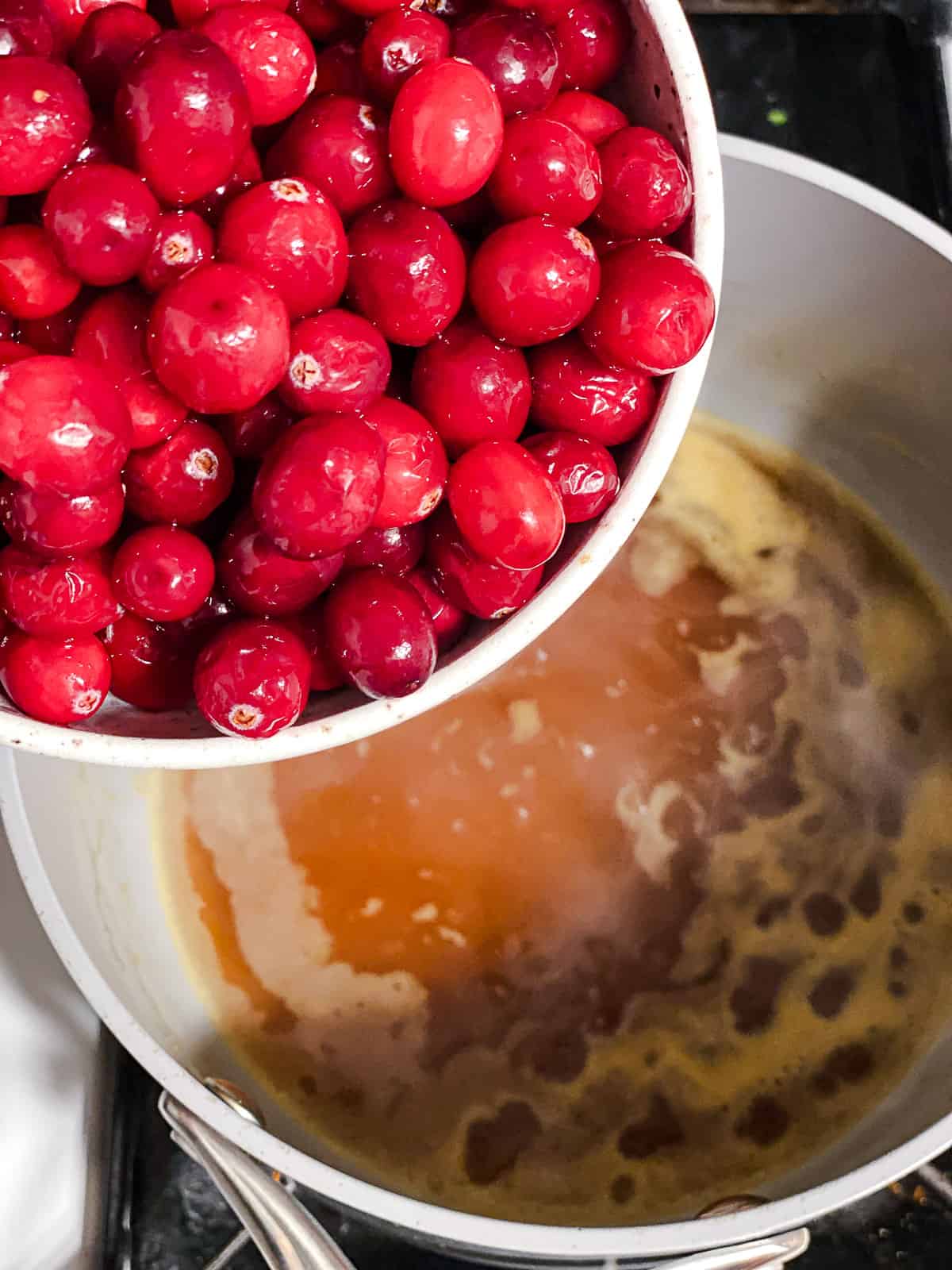 Fresh cranberries poured into a saucepan of orange juice syrup.