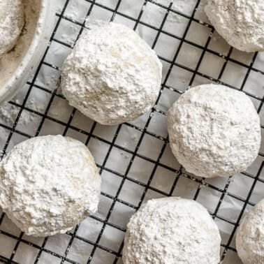 Snowball cookies without nuts coated in powdered sugar on a cooling rack.