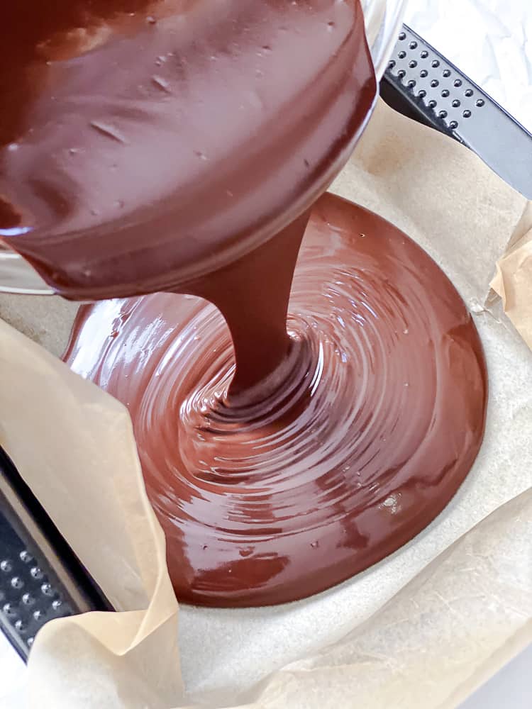 melted chocolate Biscoff fudge mixture pouring into a parchment-lined pan