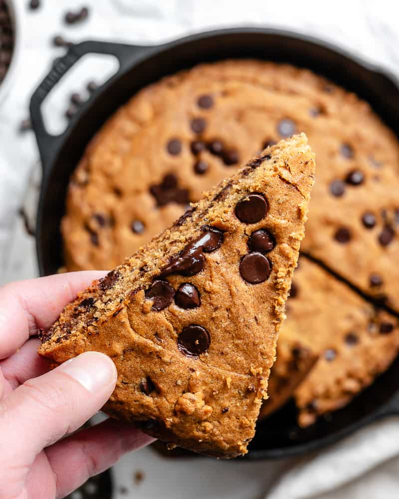 a hand holding up a slice of skillet chocolate chip cookie.