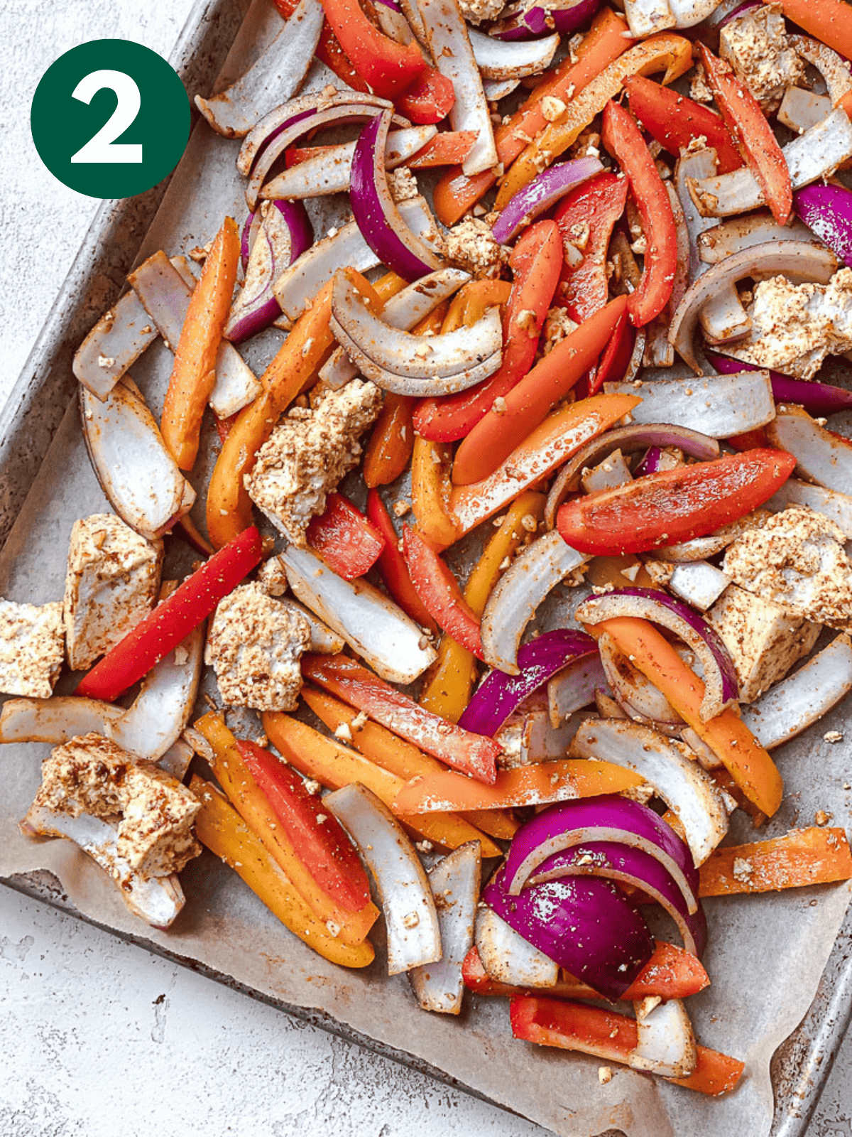 seasoned onions, bell peppers, and tofu chunks on a parchment-lined baking sheet.