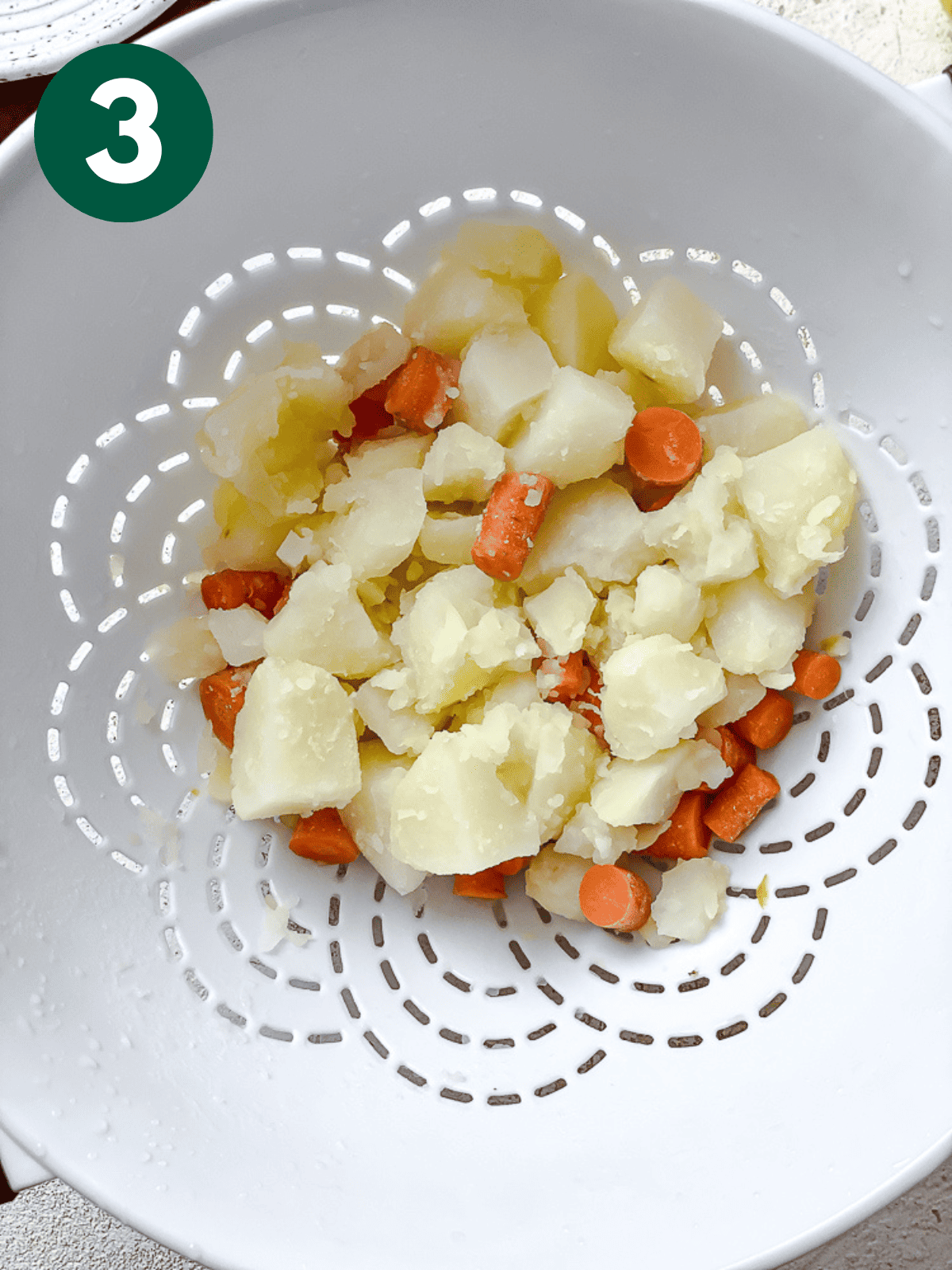 Boiled potatoes and carrots in a white strainer.