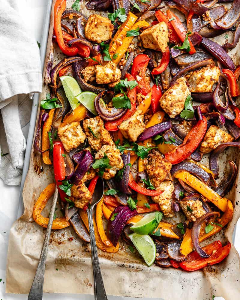 roasted taco-seasoned tofu c،ks, onion, and bell peppers on a parchment-lined sheet pan.