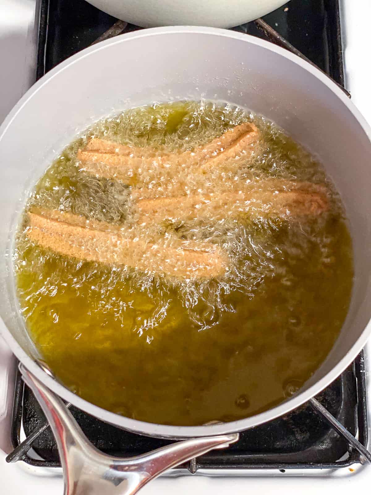 deep frying 3 vegan churros in a saucepan.