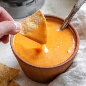 hand dipping a tortilla chip into a small bowl of vegan nacho cheese sauce.
