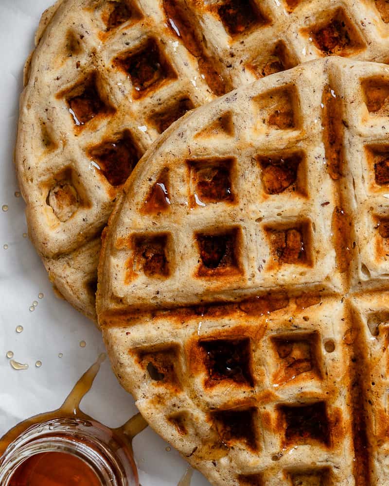 close up on cooked vegan waffles with maple syrup drizzled on top.
