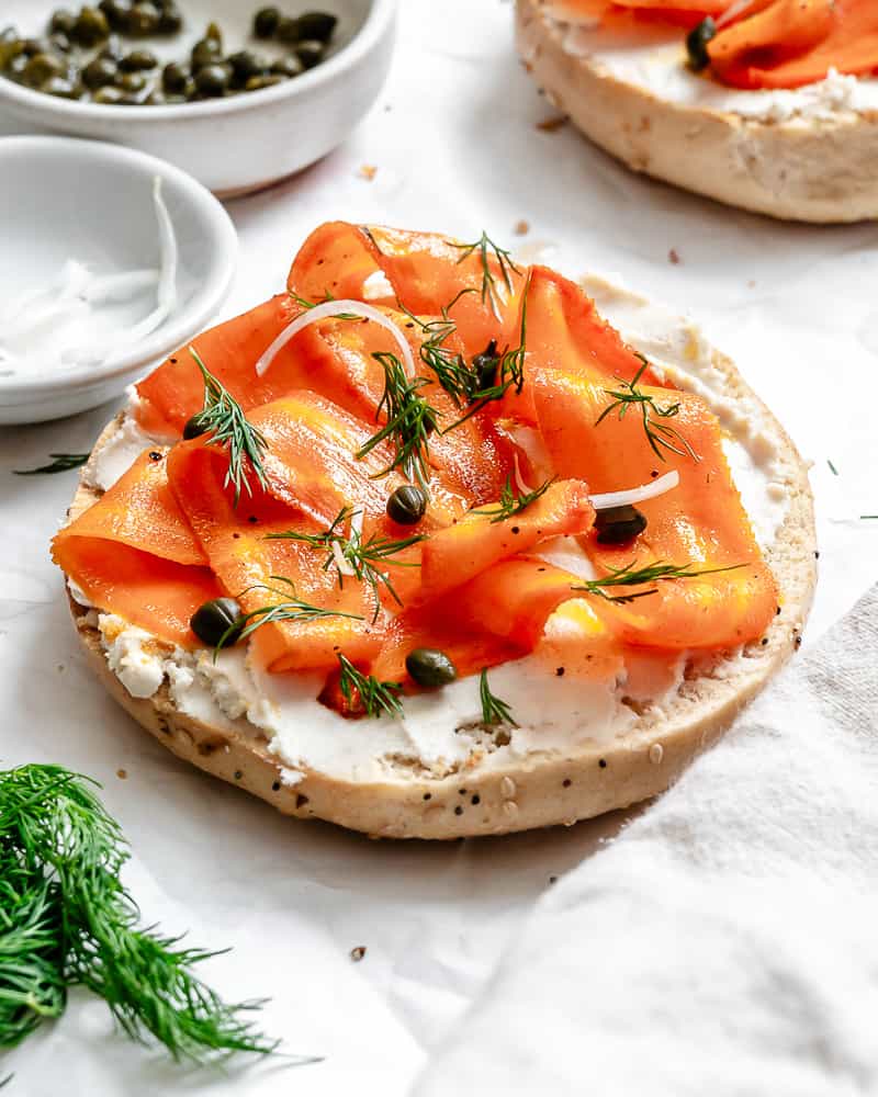completed Carrot Lox [Vegan Smoked Salmon] spread out on bagel half on a white surface