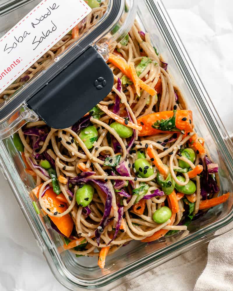 a serving of soba noodle salad in a gl، container with a lid on top labeled "soba noodle salad".