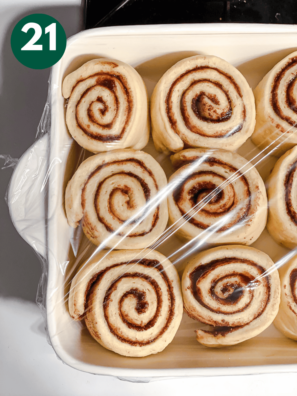 unbaked cinnamon rolls in a baking dish covered with plastic.