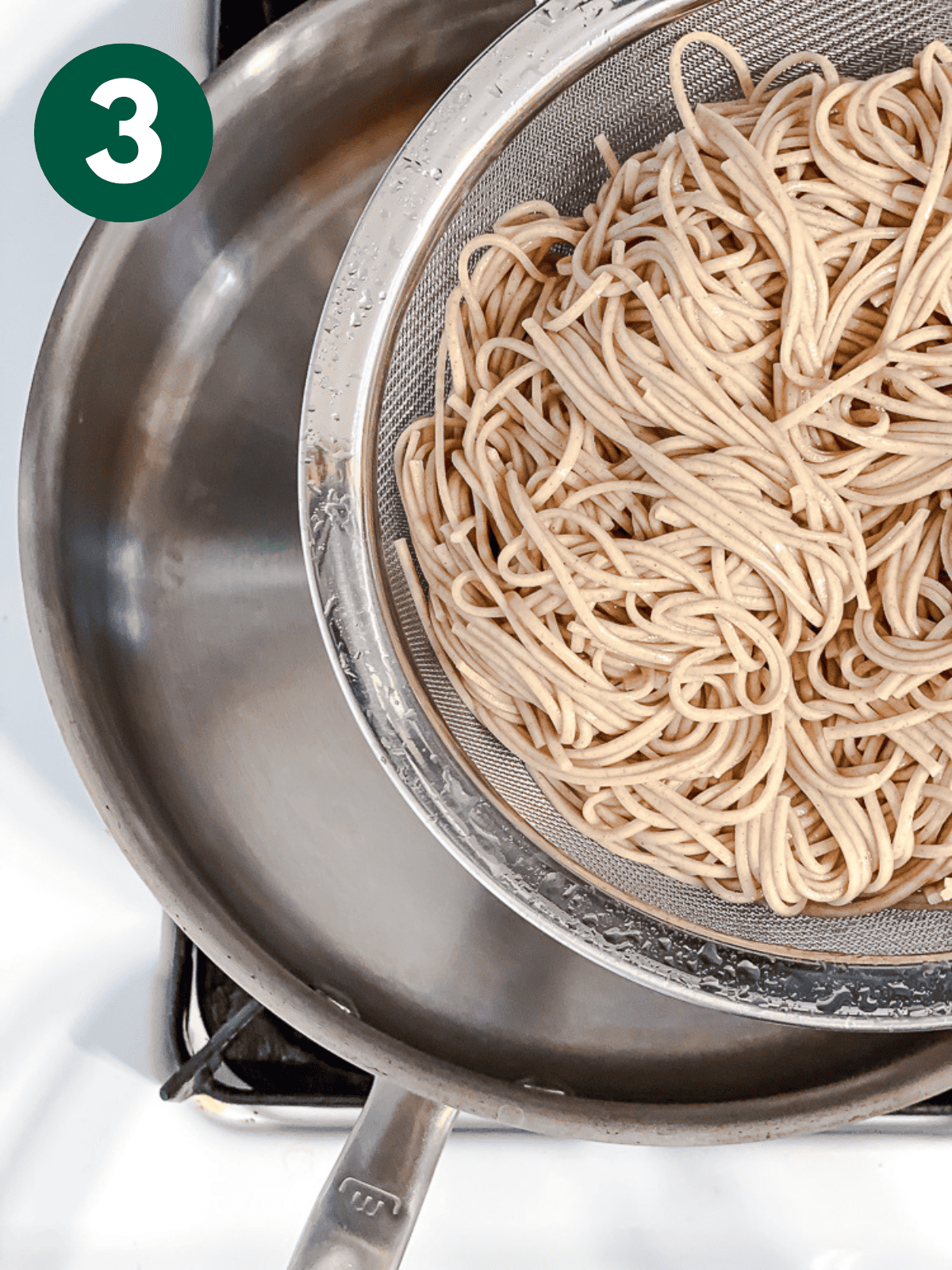draining cooked soba noodles in a metal colander.