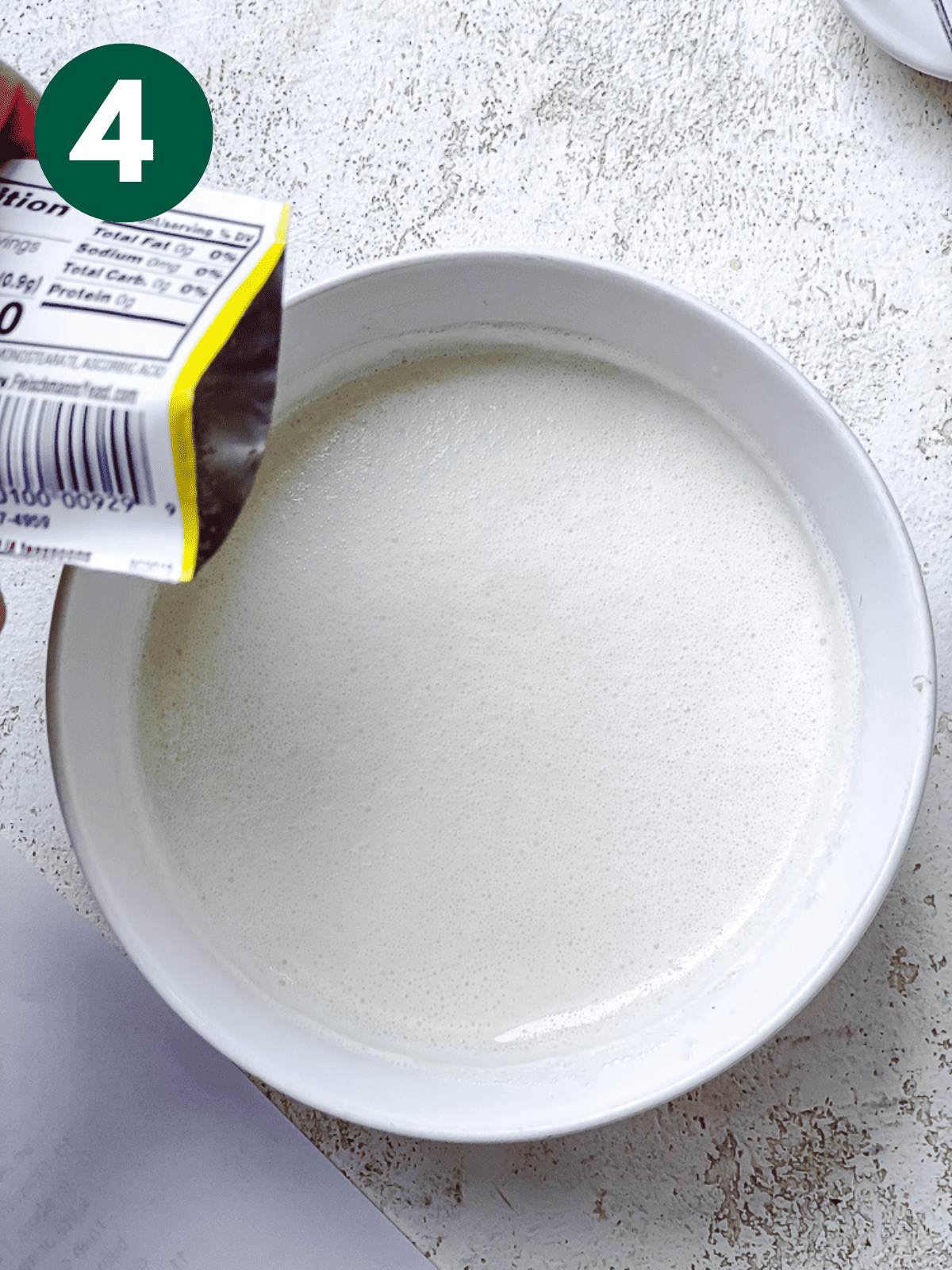 pouring a packet of yeast into a bowl of vegan buttermilk.