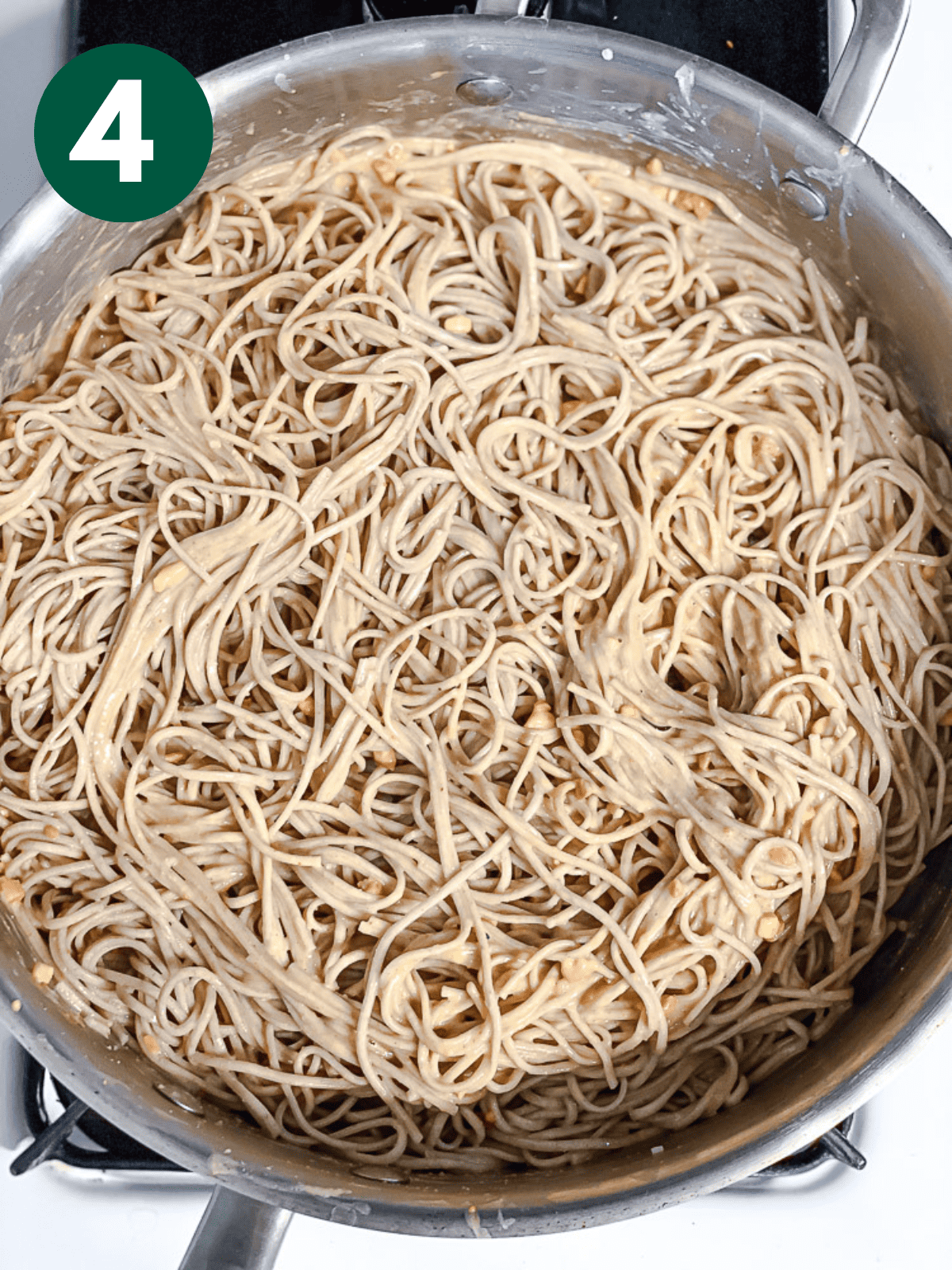 cooked soba noodles tossed in peanut sauce in a large metal ،t.