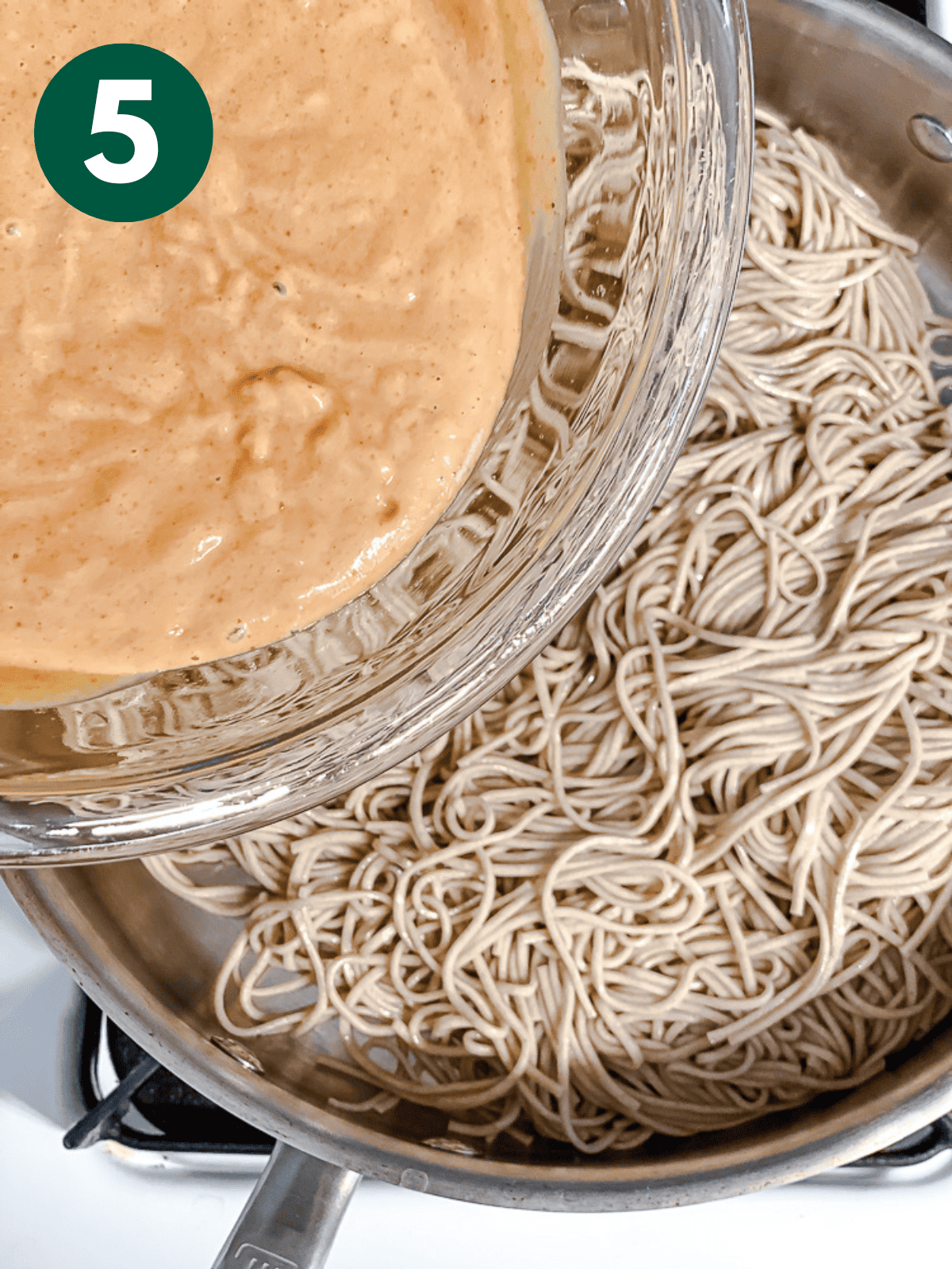 pouring peanut sauce over cooked soba noodles in a large ،.