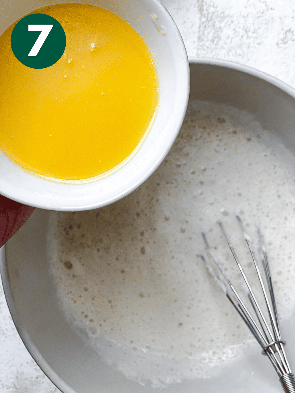 pouring melted butter into a white wet mixture in a white bowl.