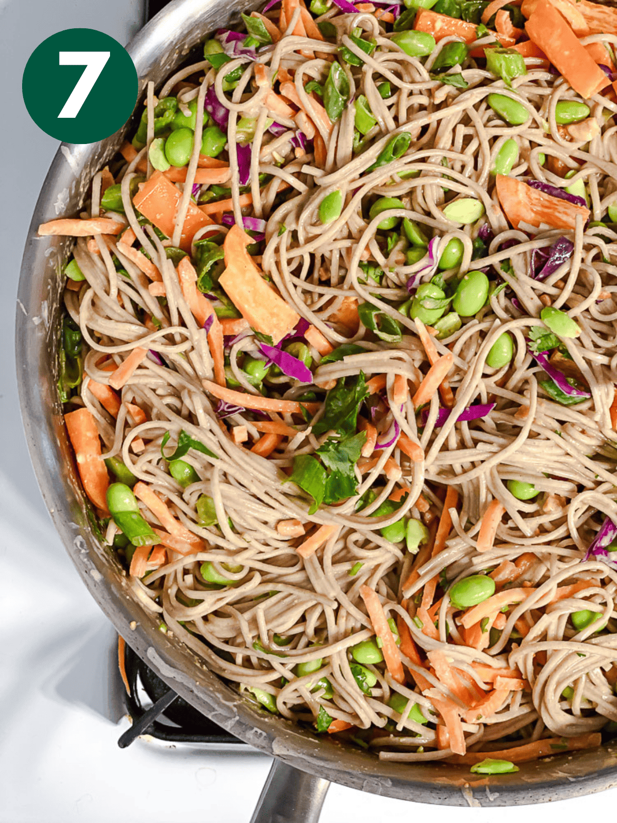 soba noodle salad tossed with peanut sauce and vegetables in a large pot.
