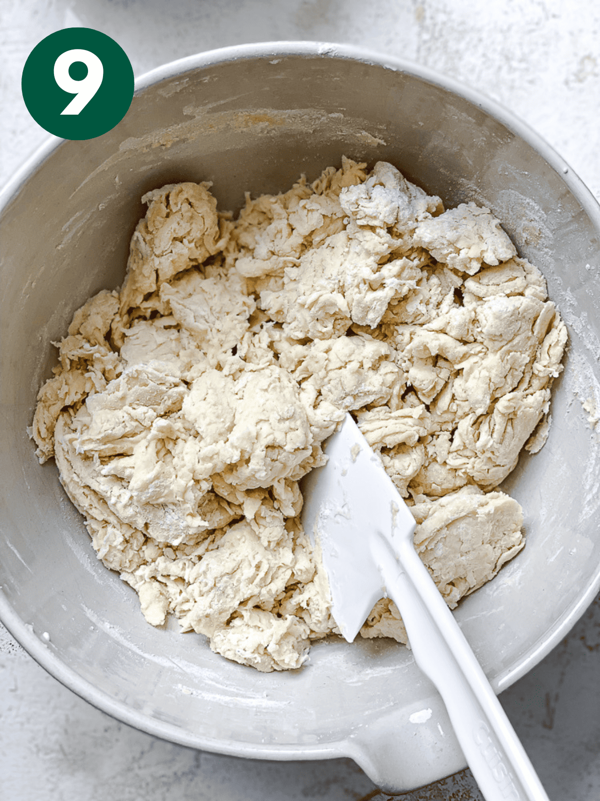 using a white spatula to stir vegan cinnamon roll dough in a large white bowl.