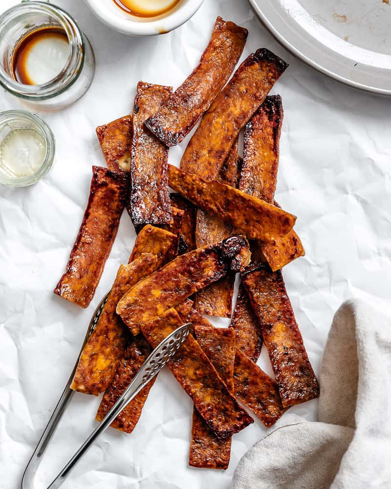 a pile of sauce-covered and baked vegan tofu bacon strips.