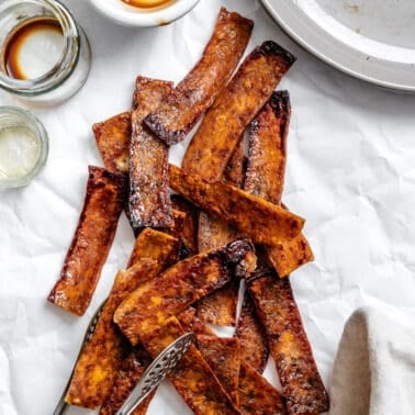a pile of sauce-covered and baked vegan tofu bacon strips.