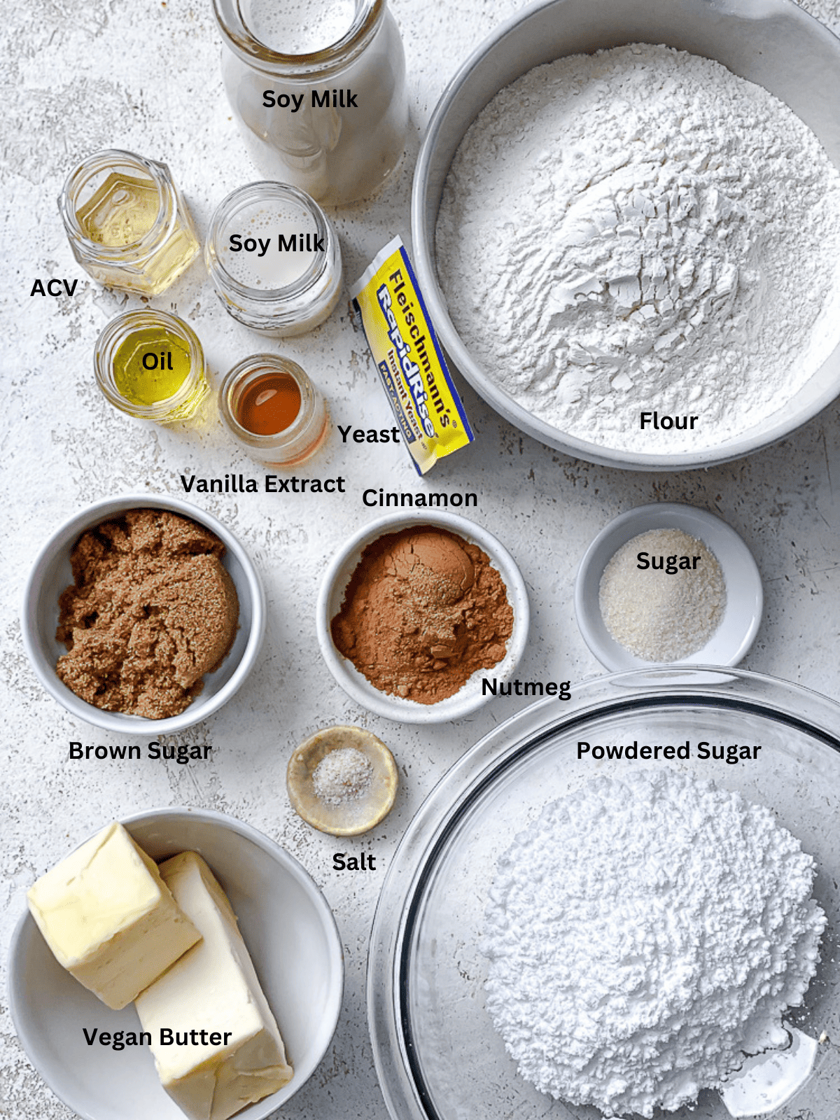 ingredients for vegan cinnamon rolls in individual bowls with labels.