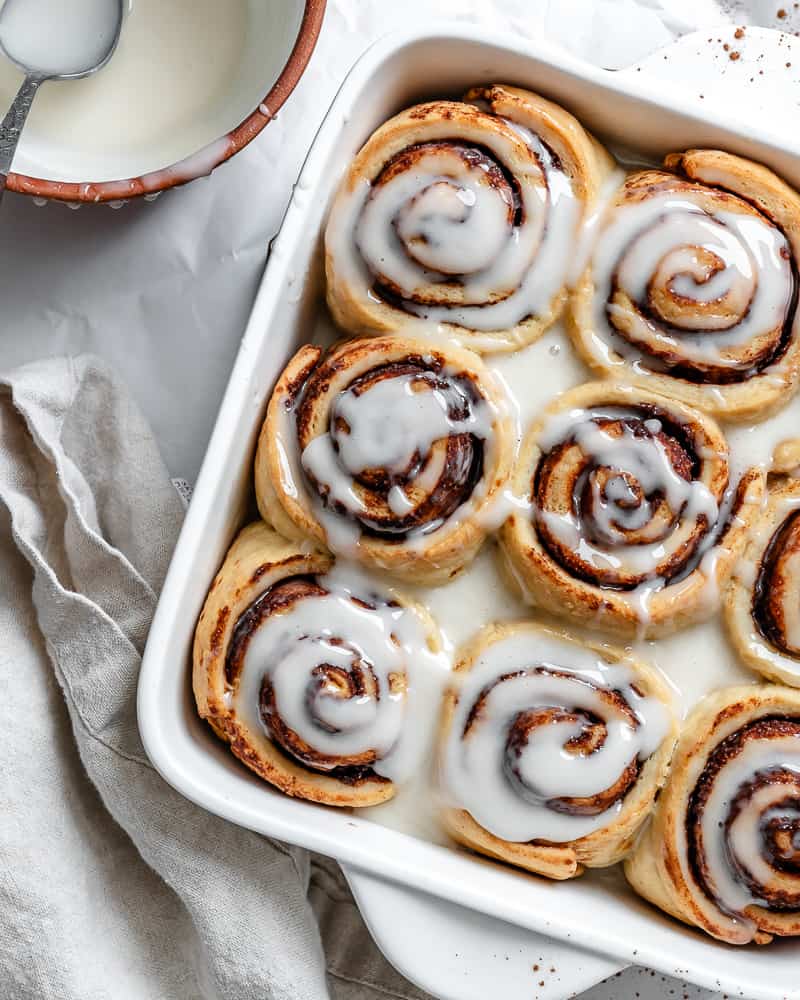 vegan cinnamon rolls in a white baking pan with vanilla icing on top.