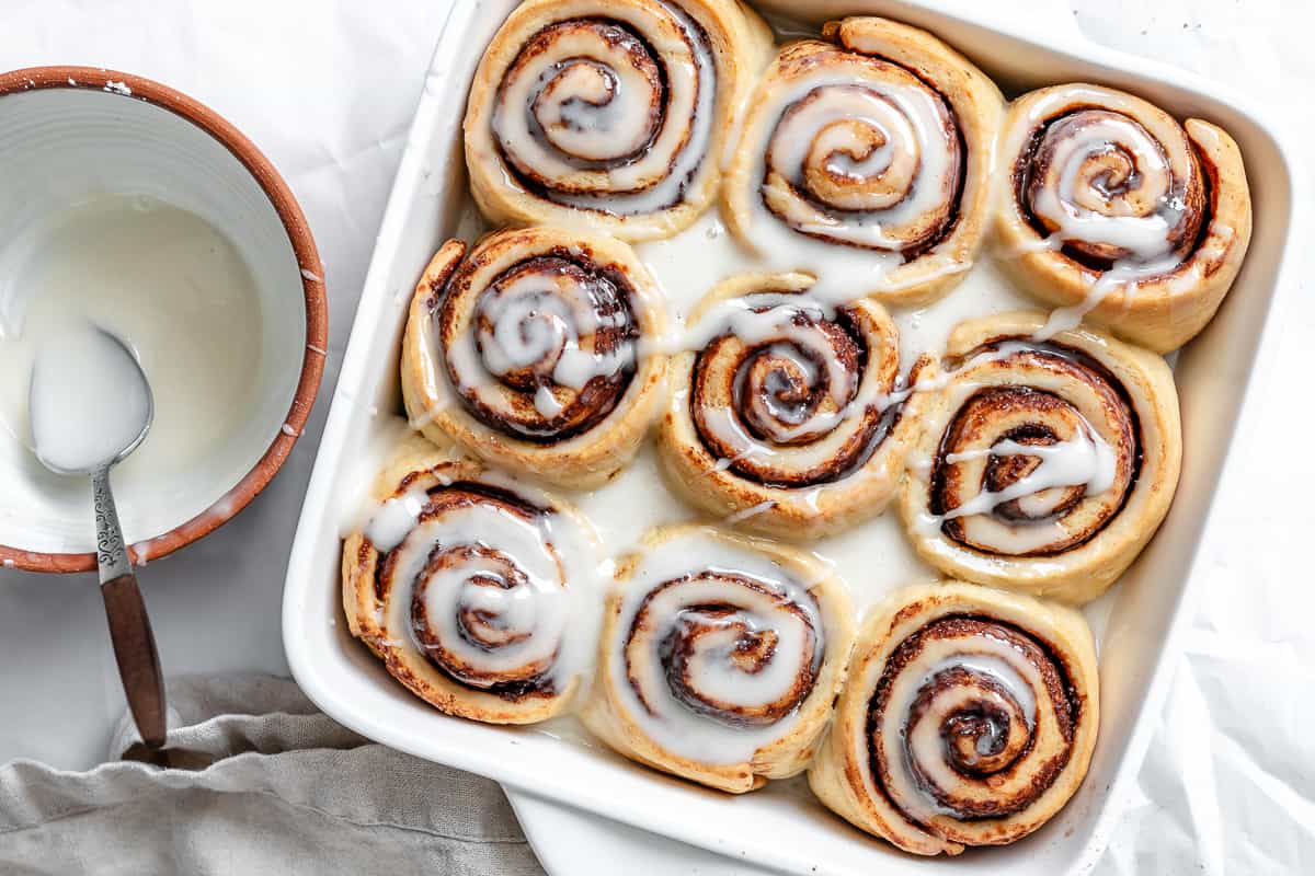 vegan cinnamon rolls in a white baking pan with vanilla icing on top.