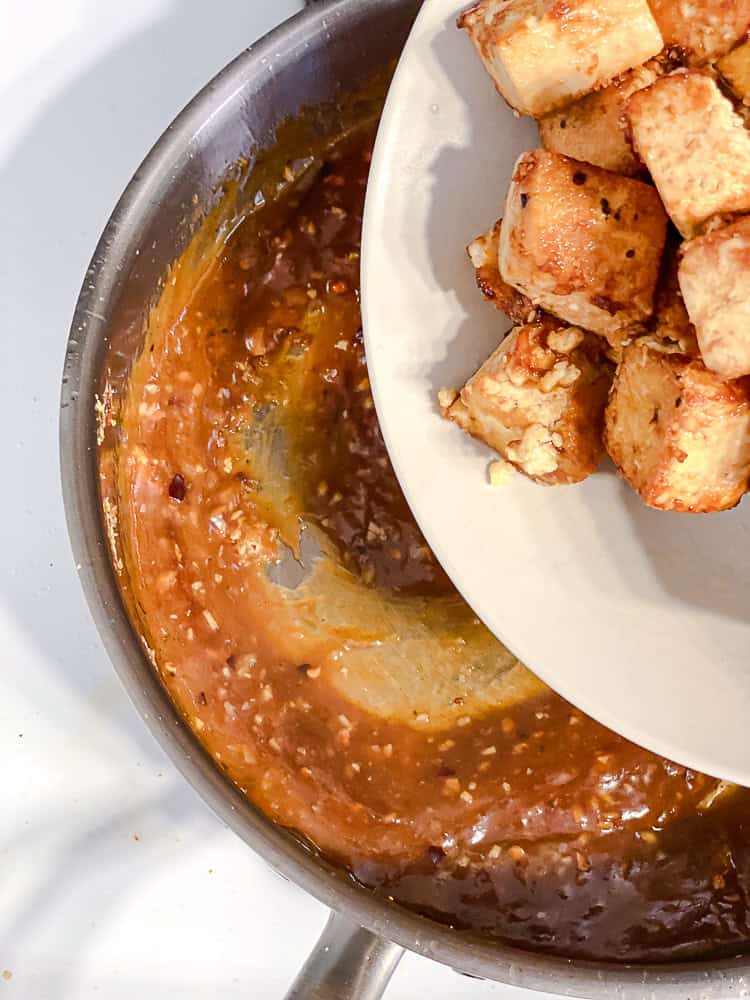 Fried tofu being added to the sauce in the pan
