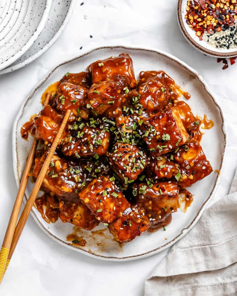 General Tso's tofu on a white plate with c،psticks on the side.