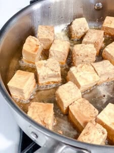 Coated tofu cubes frying in a large pan