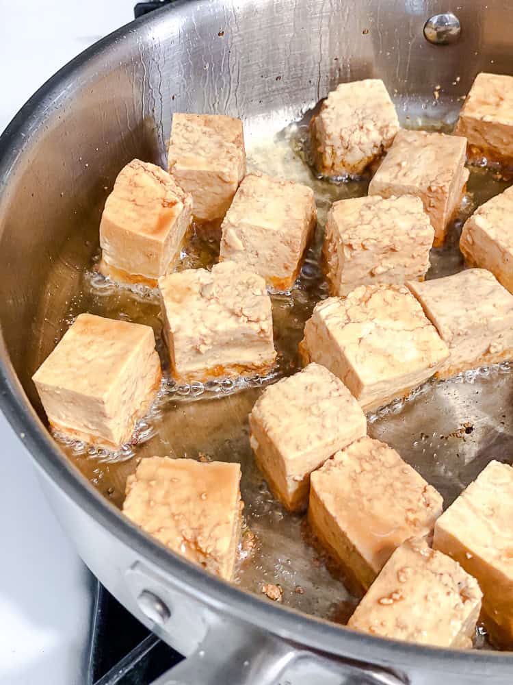 Coated tofu cubes frying in a large pan