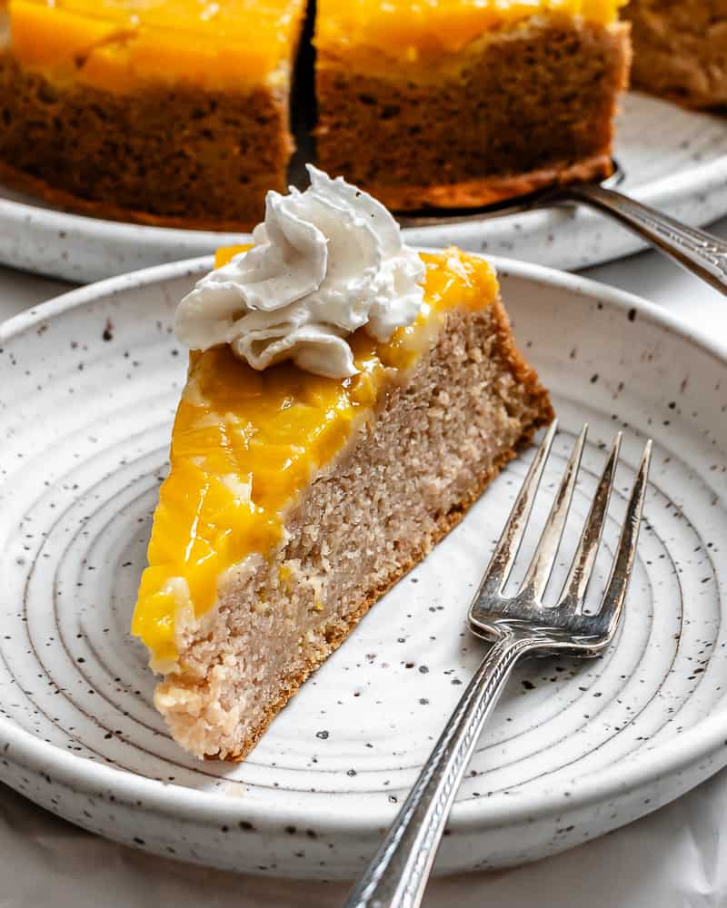 a slice of mango cake topped with vegan whipped cream on a white plate.