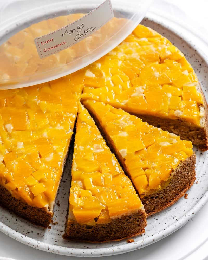 sliced mango cake on a white plate with a storage lid on top.