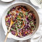 using a wooden spoon to stir ramen noodle salad in a large white bowl.