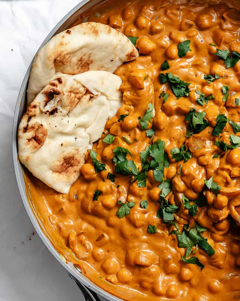 curried chickpeas in a large bowl with vegan naan tucked in the side.