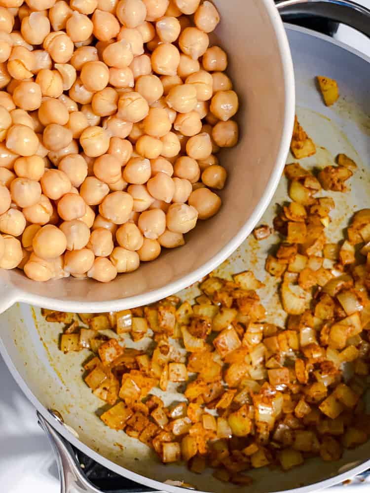 pouring chickpeas into a pan with cooked onions.