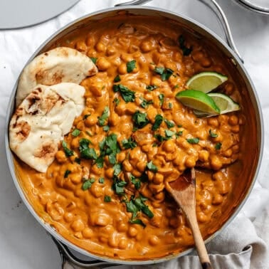 curried chickpeas in a large skillet with a wooden spoon and vegan naan tucked in the side.