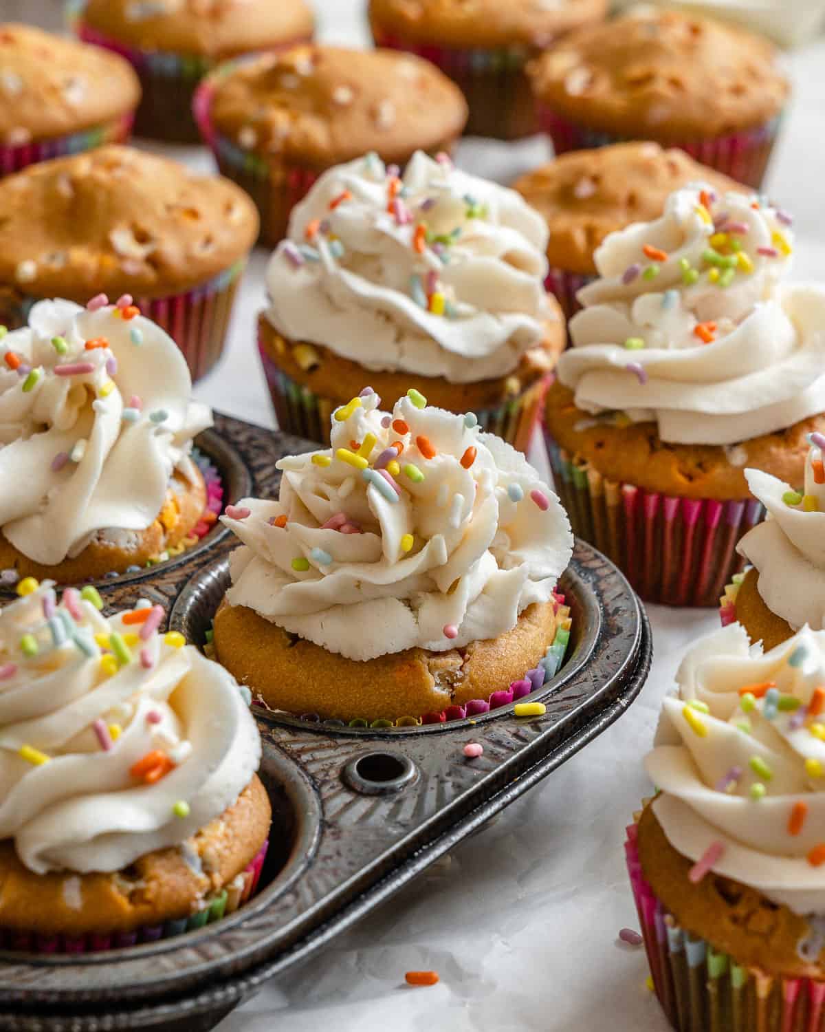 completed Vegan Funfetti Cupcakes on a white surface and cupcake tin